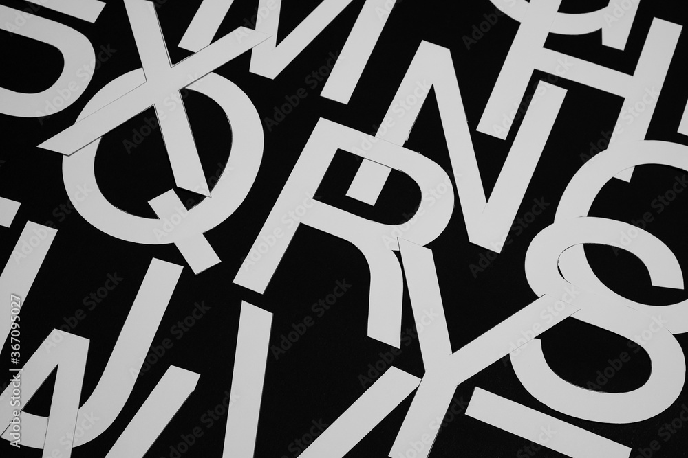 Fototapete a concept of chaos, a background consisting of white hand-cut paper letters arranged randomly on a b