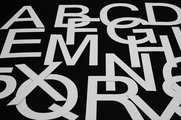 A concept of chaos, a background consisting of white hand-cut paper letters arranged randomly on a black background.