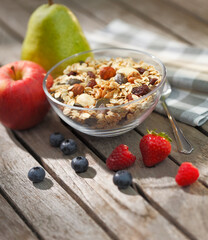 Bowl with cereals and fruits like apple, pear and strawberries on a wooden table with sun light 