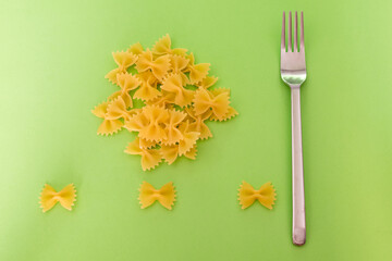 Short raw butterfly-shaped pasta on a green background with a steel seal on the side, shot from above.