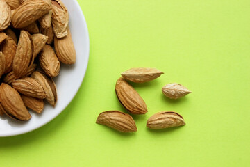 Almonds are not peeled on white plate. Yellow background. View from above. Roasted almonds for a snack. Nuts. Food. Quenching hunger. Protein. Nuts in shells. Copy space. Plate is located on the left