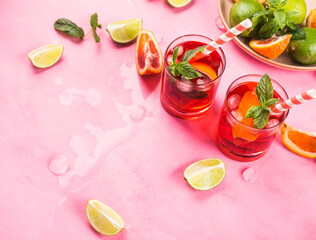 Fresh iced red cocktail with blood orange and lime on pink background garnished with mint leaves