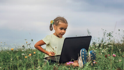 Pupil sitting on green grass outdoor and using laptop for distant studying