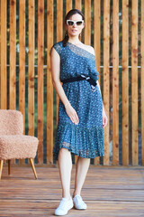 Young stylish sexy woman in summer dress standing on wooden terrace in tropical hotel, palm trees...