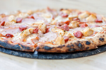 Appetizing hot Italian pizza with cheese, sausages and pieces of chicken fillet, horizontal