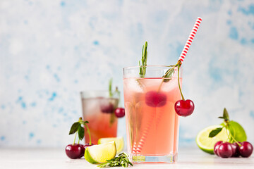 Cocktail or lemonade with cherries, lime and rosemary on a grey concrete table. Summer refreshment drink.