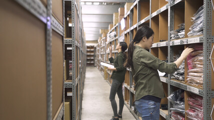 Warehouse workers working together in storehouse on relocating boxes. Female coworker with checklist in background. side view of elegant woman with mobile pad counting products on shelf in stockroom