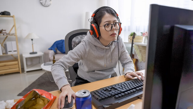 Gaming Video Games Concept. Teenage Girl Playing Football Game With Headphones On Computer. Lazy Female Enjoying Sitting In Messy Bedroom At Home Having Fun On Internet On Summer Break Holidays.