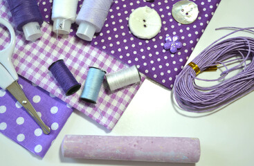 Fototapeta na wymiar Flat lay of sewing accessories including white-dotted cotton fabrics, scissors, buttons, piece of chalk, sewing spools in lilac and mauve. Scrapbooking and DIY. Hobby and needle work background. 