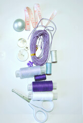 Sewing accessories including buttons, measuring tape, sewing spools in lilac and mauve against white background. Scrapbooking and DIY. Hobby, needle work