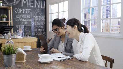 Creative work and technology. Young asian chinese women coworkers using tablet computer and laughing in cafe restaurant. two female colleagues taking break in meeting and having fun on touch pad.