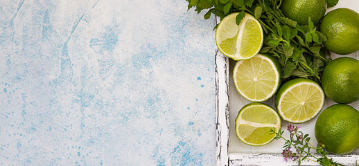 Lime and mint on light wooden tray, blue concrete background. Summer concept. Top view.