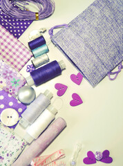 Obraz na płótnie Canvas Flat lay of sewing accessories including white-dotted and floral cotton fabrics, buttons, piece of chalk, sewing spools in lilac and mauve against ecru background. Scrapbooking and DIY. Hobby