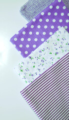 A set of white-dotted and floral cotton fabrics in lilac and mauve with white space for text. Vertical view. Scrapbooking and DIY. Hobby and needle work background. 