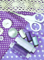 Fototapeta na wymiar Sewing accessories including white-dotted cotton fabrics, scissors, buttons, sewing spools in lilac and mauve. Scrapbooking and DIY. Hobby and needle work background. 