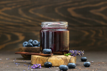 Glass jar and spoon with delicious blueberry jam with fresh berries, lavender and rosemary on dark...