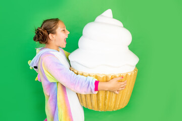 a little girl on a green isolated background in a bright suit holds a huge cake. Space for text....