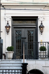 Vintage black double door with lanterns, flower pots and decorative forging. New York. USA.