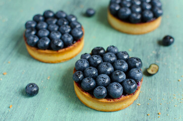 Mini tarts decorated with fresh blueberry on green background