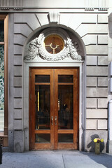Wooden vintage double arched entry door decorated with floral plaster, round window and rustication. New York. USA.
