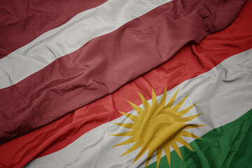 waving colorful flag of kurdistan and national flag of latvia.