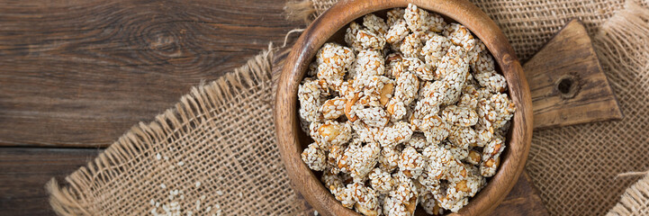 Roasted peanuts in honey syrup and sesame. Peanuts in sesame seeds in a wooden bowl on a brown wooden table. Top view with space for text. Banner