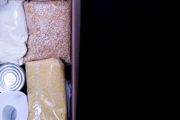 Cardboard box with Food supplies crisis food stock for quarantine on the black background. Rice, canned food, toilet paper. Food delivery. coronavirus quarantine concept. Copyspace