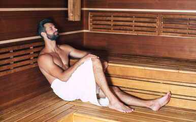 Young handsome beard man in the bath towel is relaxing in the hot sauna while vacation