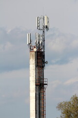Old dirty concrete industrial chimney with rusted metal steps on one side and security fence on top...