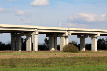 Fototapeta na wymiar Side view of wide concrete bridge on top of multiple strong thick support columns with dirty old wind direction and speed red and white indicator flag and two white traffic cameras rising high above l