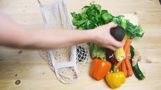 Male hands are packing, putting fresh vegetables in a cotton string bag. No plastic, grocery packaging, grocery delivery.