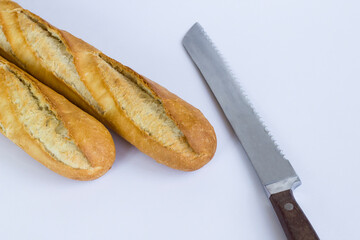 Fresh baguette breads on white surface with knife,above view.