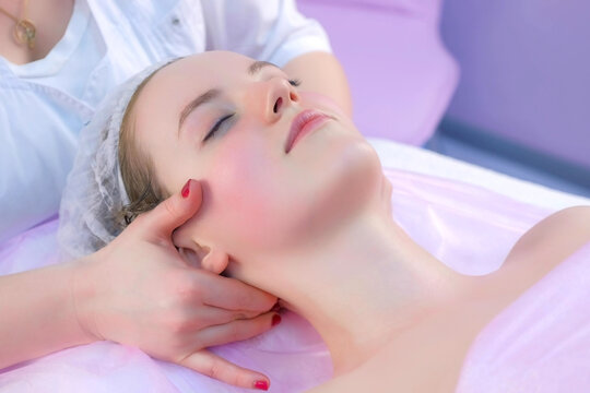 Cosmetologist massagist doctor making myoplastic neck massage to young woman, closeup portrait. Beauty spa procedure in cosmetology clinic. Doctor stroking and rubbing neck of young girl.