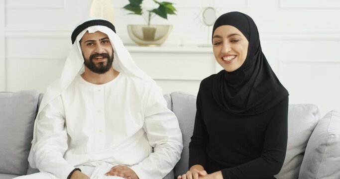 Arabs muslim happy couple talking to camera, waving with hands. Having videochat. Male and female Arabians videochatting on webcam. Middle East. Male in kandura and woman in hijab. Traditional outfits