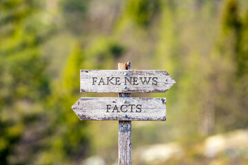 fake news facts text carved on wooden signpost outdoors in nature. Green soft forest bokeh in the background.