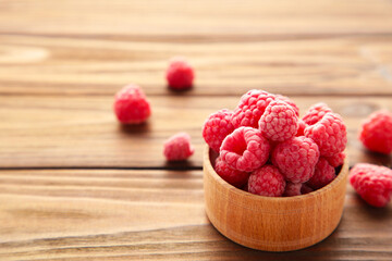 Ripe raspberries in wooden bowl on brown background. Top view