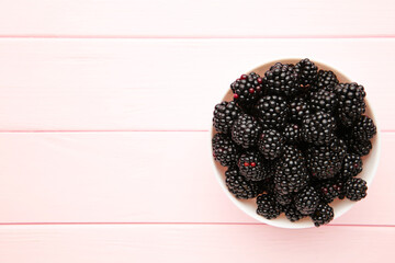 Blackberries in a bowl on pink wooden table.