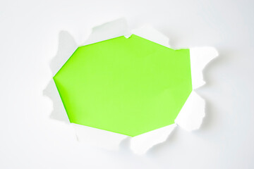 Torn oval hole in white paper with torn edges and green background. Copy space, paper texture.