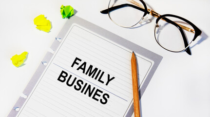 In a white notebook is a FAMILY BUSINES inscription, next to pencils, glasses, graphs and diagrams.