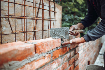 Professional worker using pan knife for building brick walls with cement and mortar.