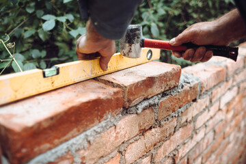 professional construction worker laying bricks and building brick walls in industrial site. Detail...