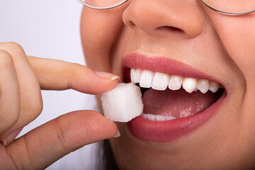 Beautiful woman mouth with big white teeth bites on a white sugar cube