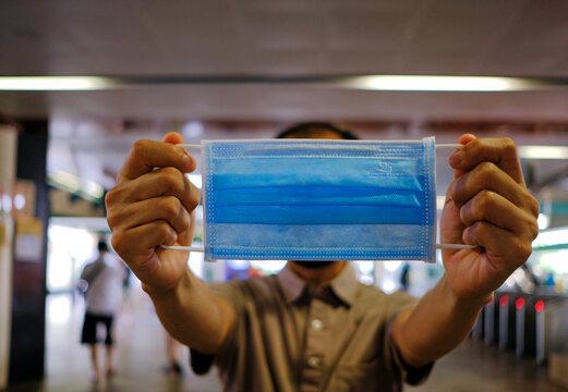 Man holding up surgical mask in train station. Now mandatory to wear masks outside of homes in public places during lockdown period, coronavirius covid-19 outbreak