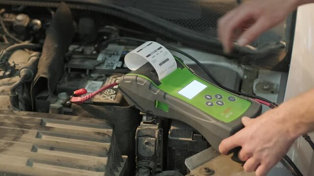 Auto service worker checking voltage on car battery. Service engineer working in car service station