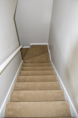 Top view of wooden stair covered by brown carpet in a modern white house with white wall