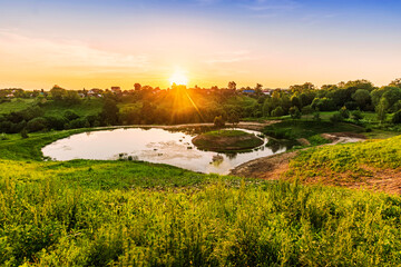 Scenic view at beautiful spring sunset with reflection on a shiny lake in shape of heart, grass,...