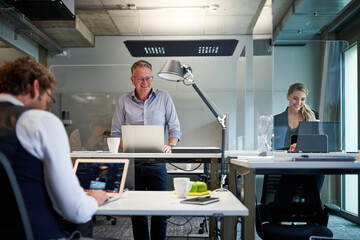 Smiling business colleagues using laptops while working at creative office with glass shields...