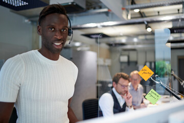 Portrait of smiling businessman standing by glass shield with reminder notes at creative office during coronavirus