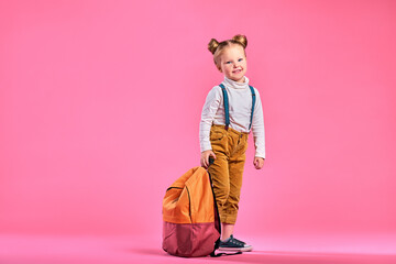 Full length portrait of a schoolgirl standing on pink background