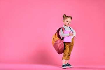 Little school girl with a notebook and backpack - isolated over a pink background